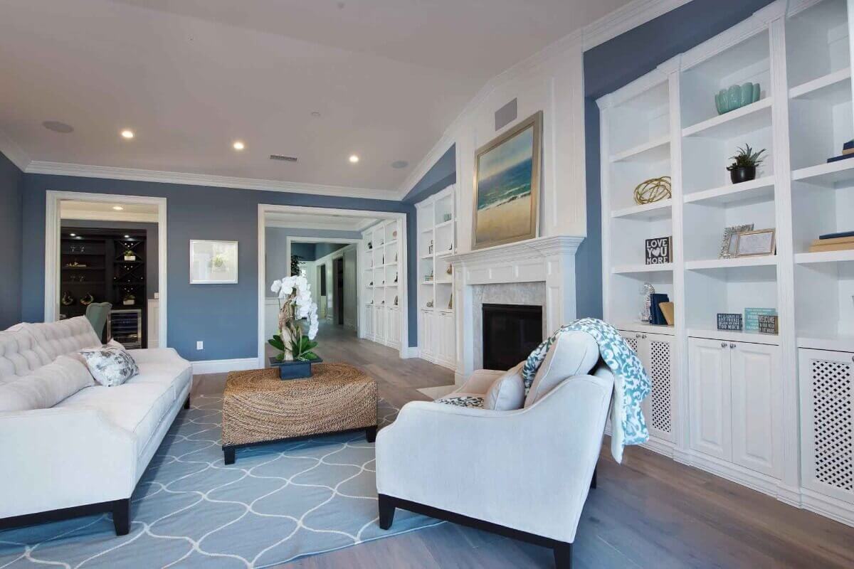 A blue and white living room with a fireplace and recessed bookcases, part of a home remodel by Los Angeles design-build firm A-List Builders.