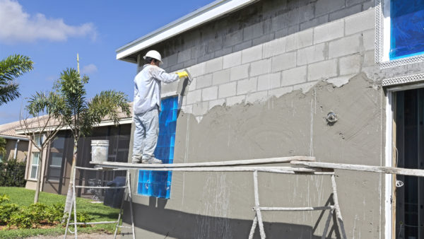 Worker standing on makeshift platform applies stucco coating to exterior wall