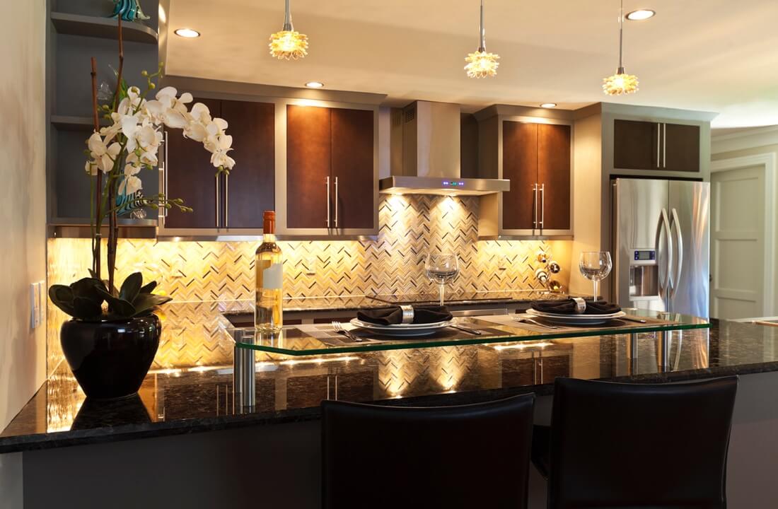 Pendant and ceiling lights reflect off stone counters and tile backsplashes, part of a kitchen remodel in Los Angeles, California by A-List Builders.