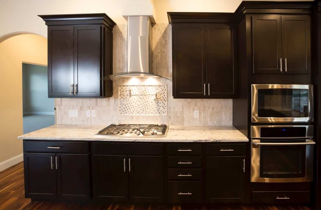 A range top and suspended fume hood surrounded by dark wooden cabinets, part of a kitchen remodel in Los Angeles, California by A-List Builders.