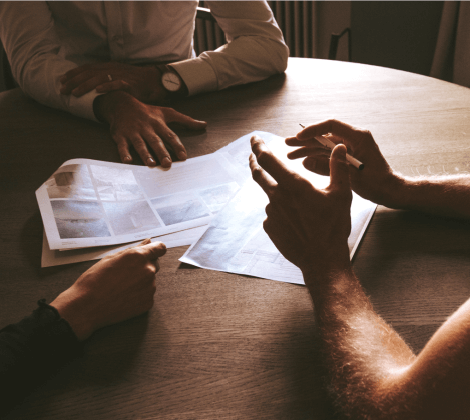 Three people's hands and arms at table discussing plans