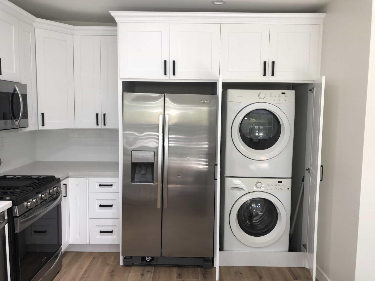 Laundry machines are hidden behind elegant cabinetry next to a refrigerator in a kitchen at a home in Woodland Hills, CA, part of a remodel by A-List Builders.