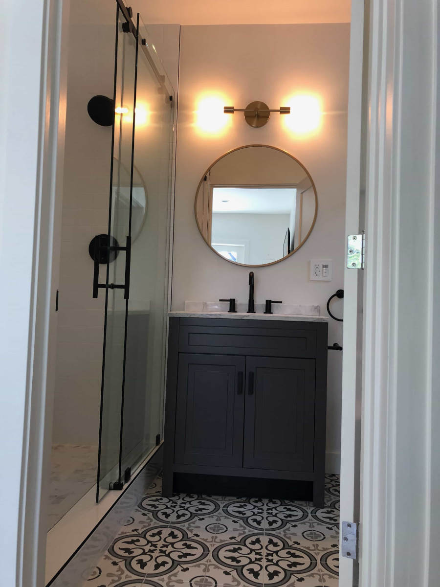 A wood and marble bathroom vanity with round mirror and glass wall shower, part of a Beverlywood, CA home remodel by LA design-build firm A-List Builders.