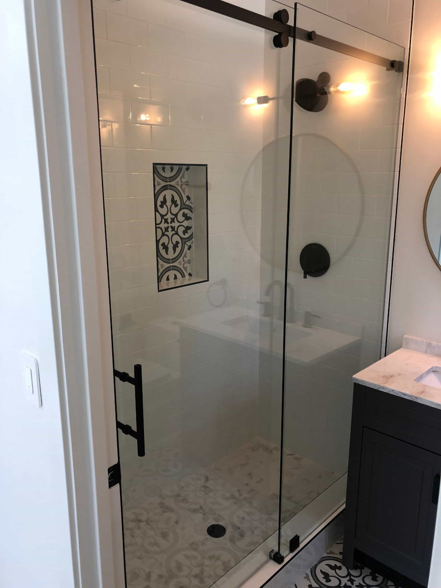 A white shower with glass wall and striking black handles and fixtures, part of a home remodel in Beverlywood, CA by LA design-build firm A-List Builders.
