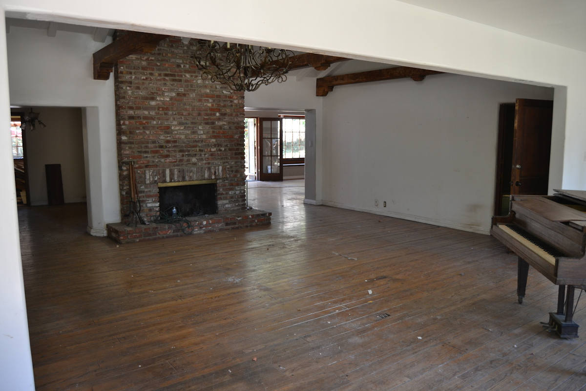 A piano and brick fireplace in a large family room with hardwood floors in Sherman Oaks, CA prior to being gutted for remodeling by A-List Builders.