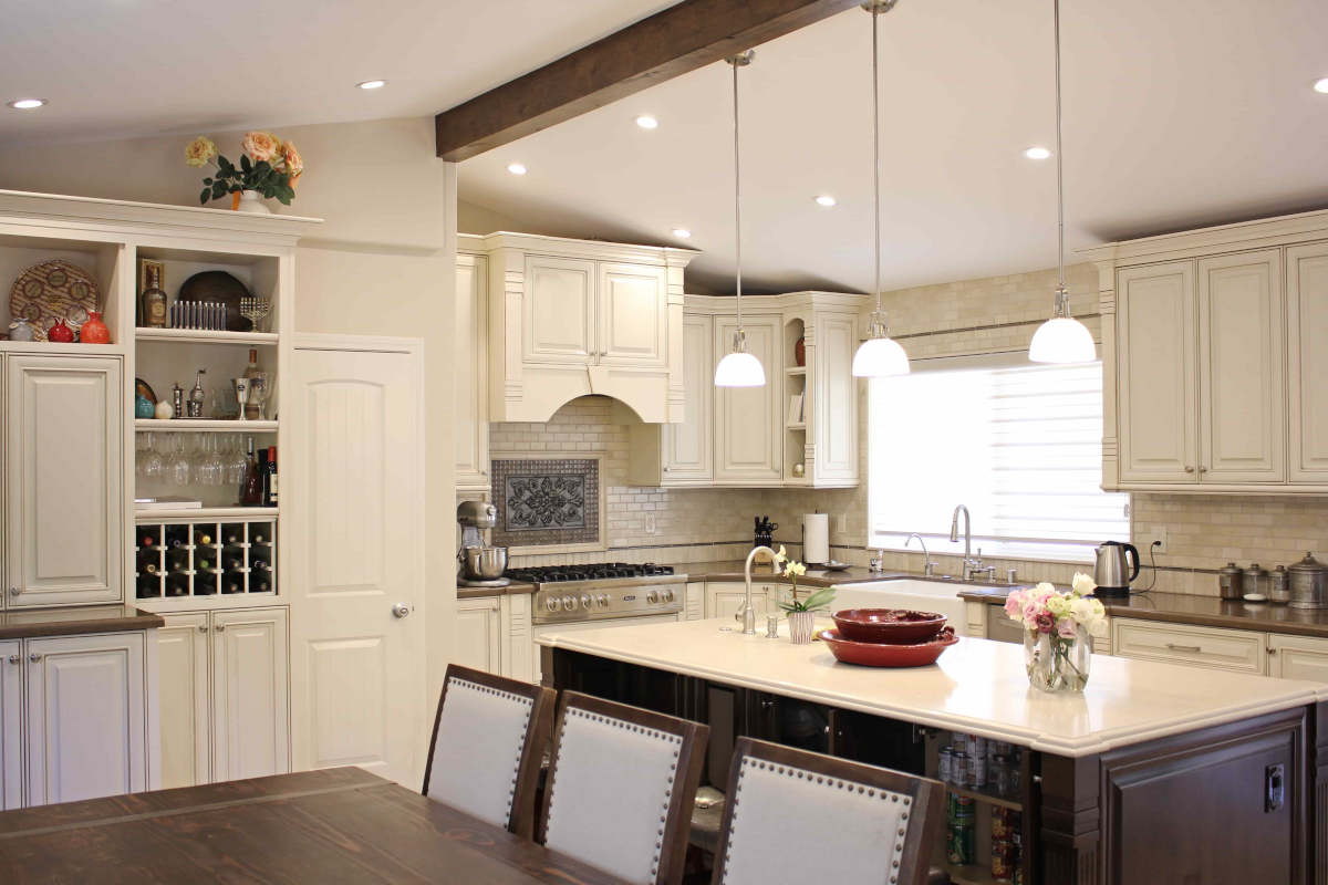 A newly remodeled kitchen in Sherman Oaks, CA by A-List Builders, with pendant lights hanging from an exposed beam over a center island, and white cabinetry.