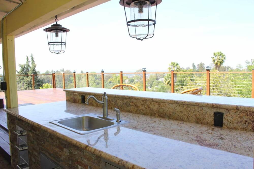 An outdoor wet bar, covered by overhang with vintage lighting, on a deck at a home in Studio City, CA, part of a remodel by design-build firm A-List Builders.