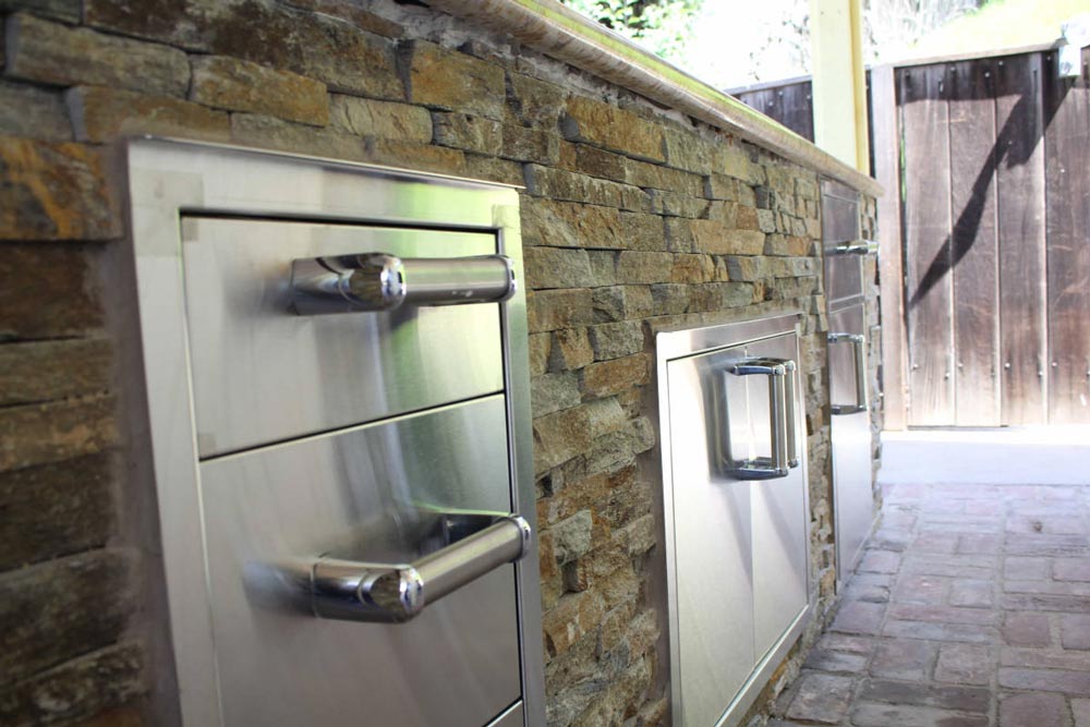 Stainless steel doors and drawers in an outdoor stone wall, part of a home remodel in Studio City, CA by Los Angeles design-build firm A-List Builders.