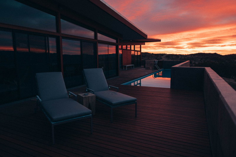 Pool lounge chairs sitting on a deck at sunset.