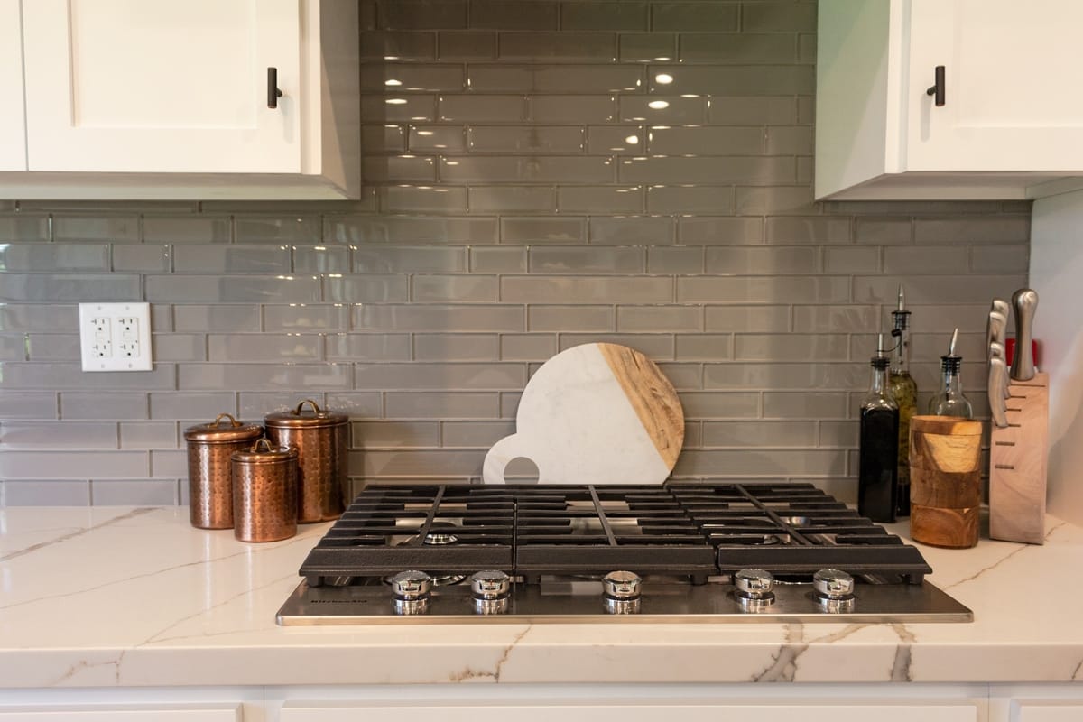 A range top framed by marble counters and tile backsplash, part of a complete home remodel in Porter Ranch, California by design-build firm A-List Builders.