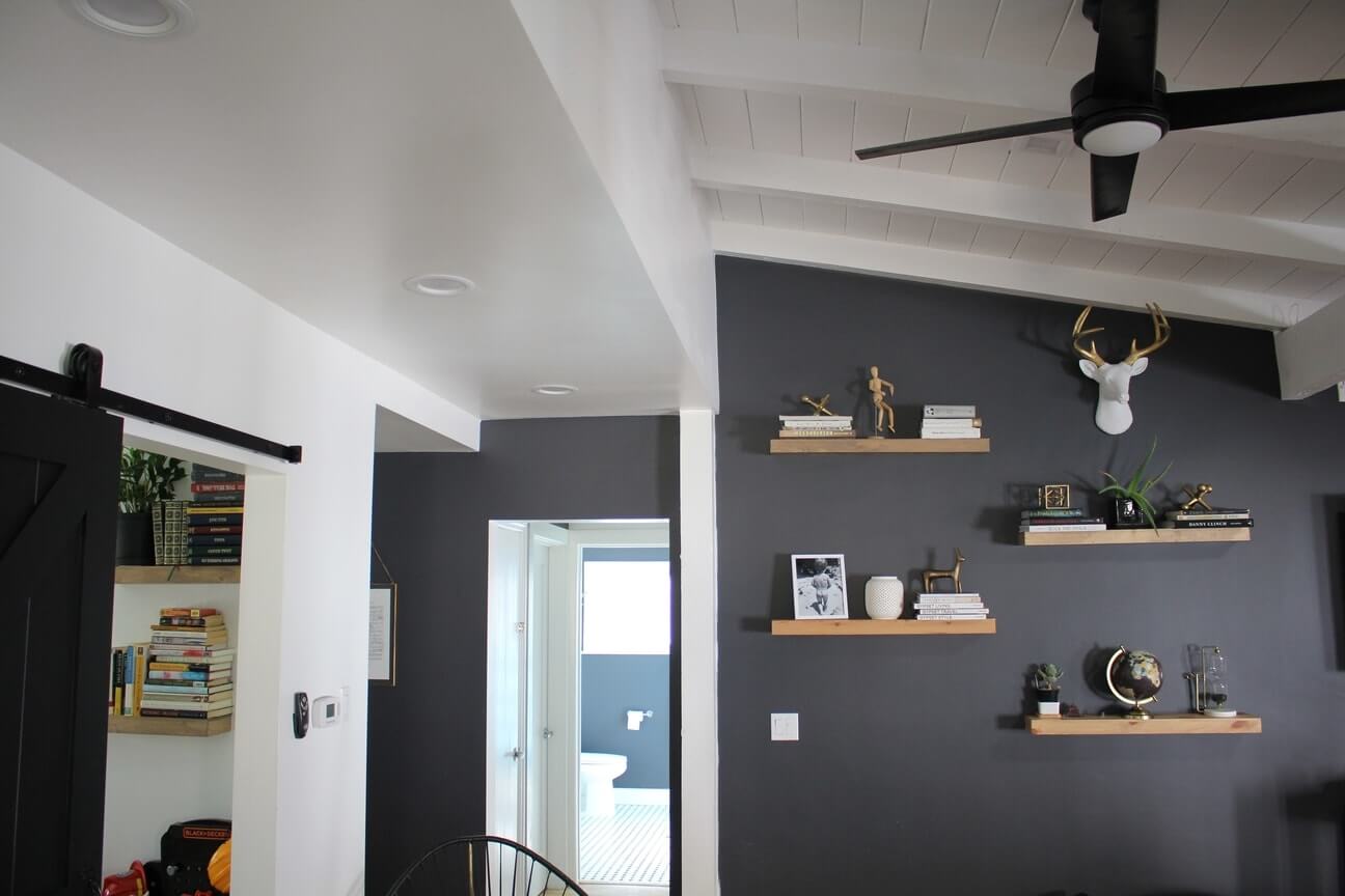 A cozy, white and dark gray living room with simple wooden shelves built into the wall, and a slanted ceiling, part of an LA home remodel by A-List Builders.