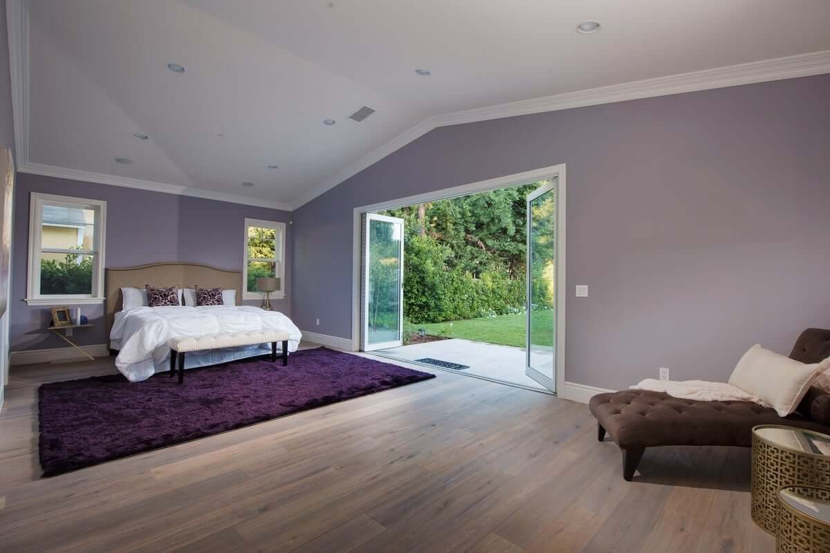 A light purple master bedroom with sliding glass wall and hardwood floors, part of a home remodel by Los Angeles design-build firm A-List Builders.