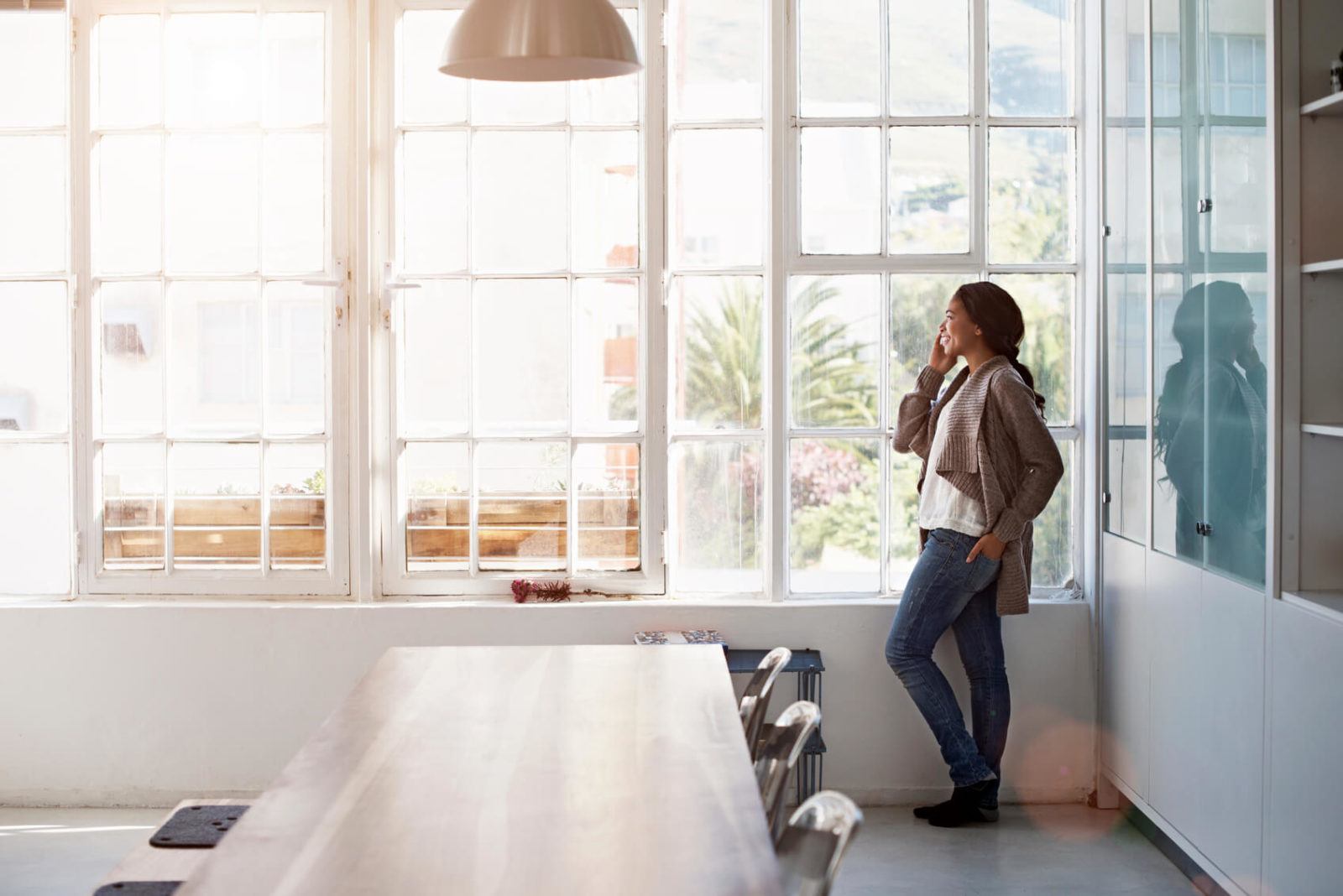 Woman on phone call, standing in front of tall kitchen windows